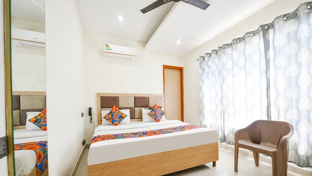 A hotel room with a bed, a chair, a ceiling fan, and a window with curtains. - Fabescape Panchkula Motels (Dera Bassi)