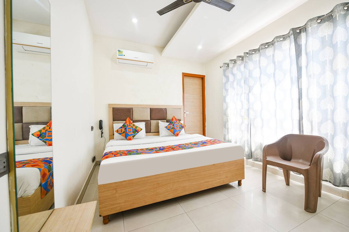 A hotel room with a bed, a chair, a ceiling fan, and a window with curtains.