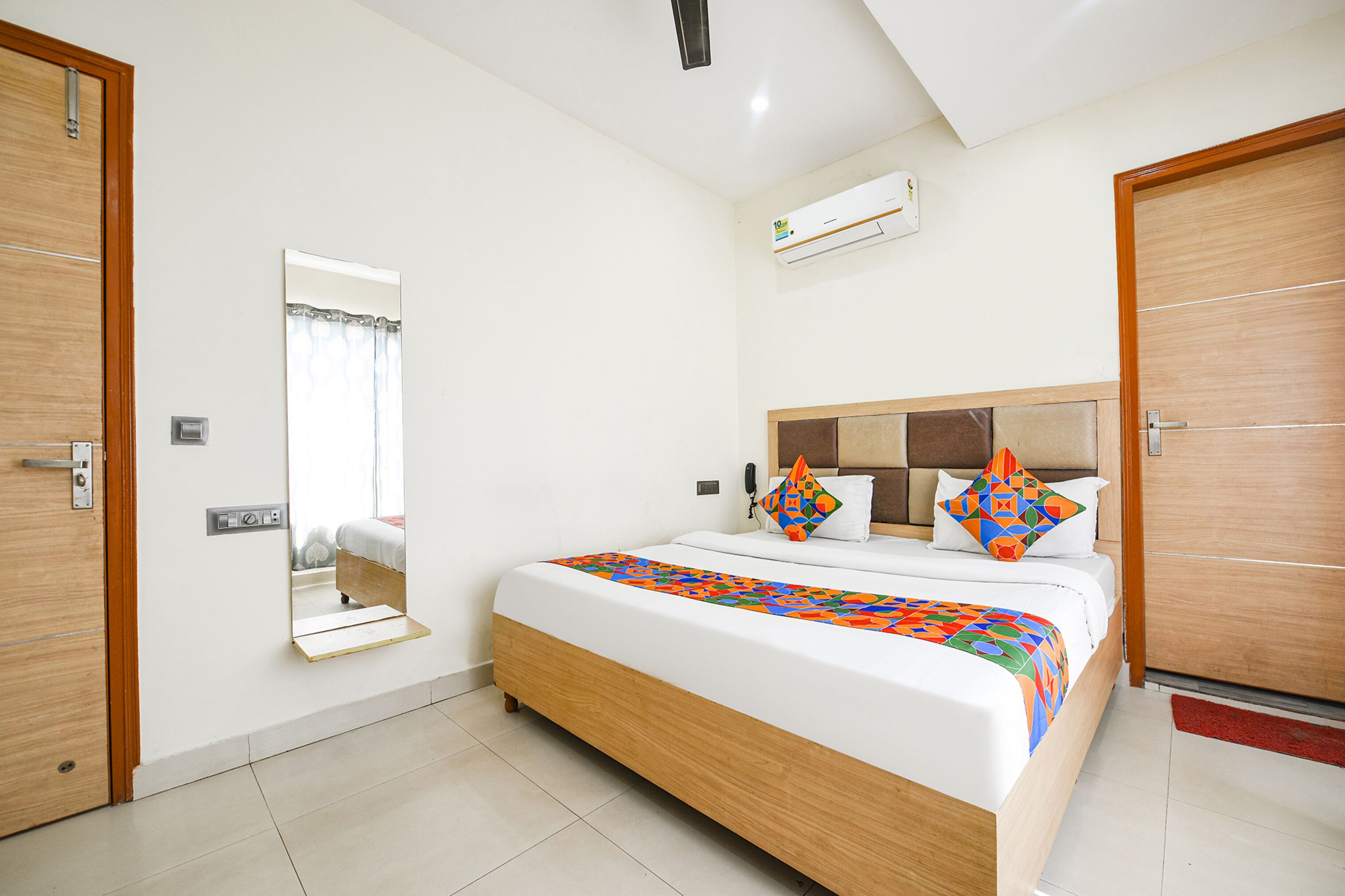 Een hotelkamer met een houten bed, een spiegel, een airconditioning en een rode deurmat.