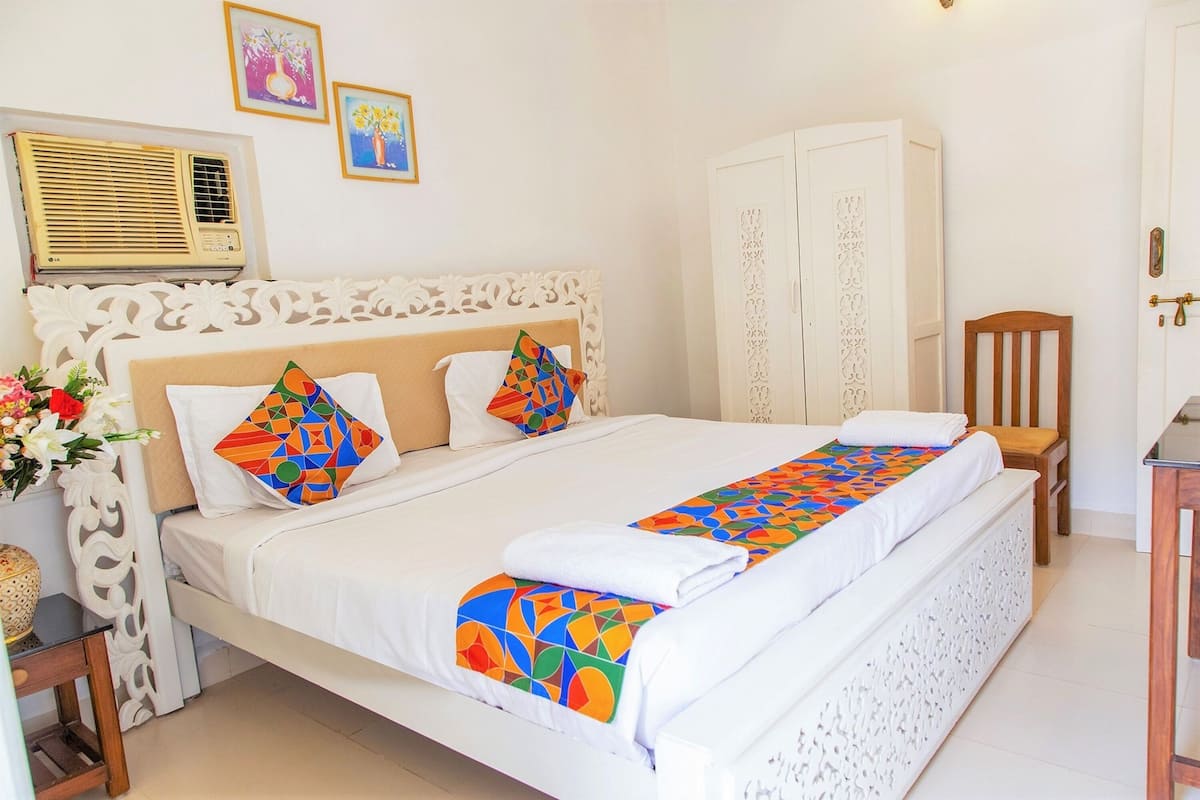 A neatly made bed with colorful geometric pillows, a white headboard, and a decorative wall panel.