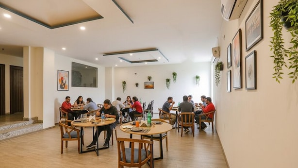 A dining area with round tables and chairs, ceiling lights, and wall-mounted plants. - Fabhotel F9 Sector 58 (Noida)