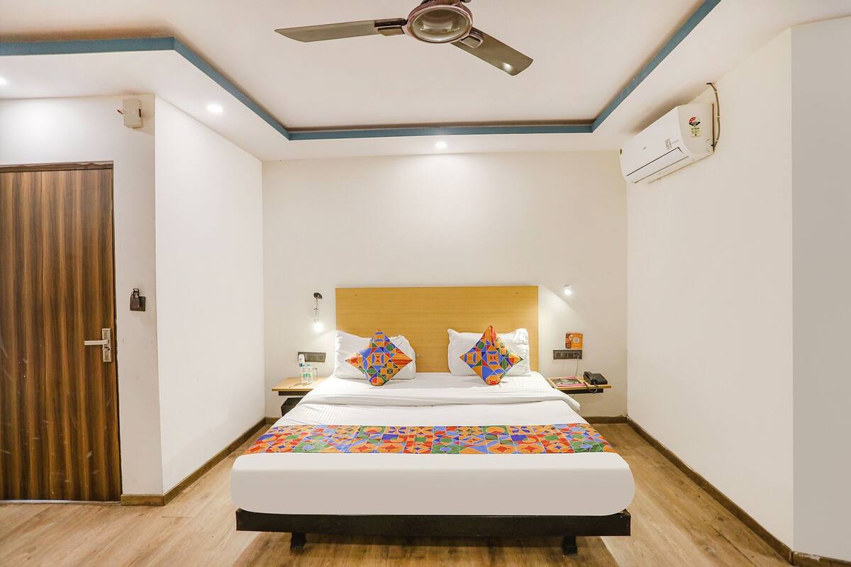 A hotel room with a bed, a ceiling fan, a wooden door, and a wall-mounted air conditioner.