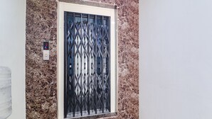A door with a metal security gate, set in a room with a marble wall. - Fabhotel Lotus Park (Visakhapatnam)