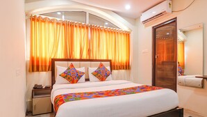 A neatly made bed with a colorful bedspread, a bedside table with a lamp, and a window with orange curtains. - Fabhotel Lotus Park (Visakhapatnam)