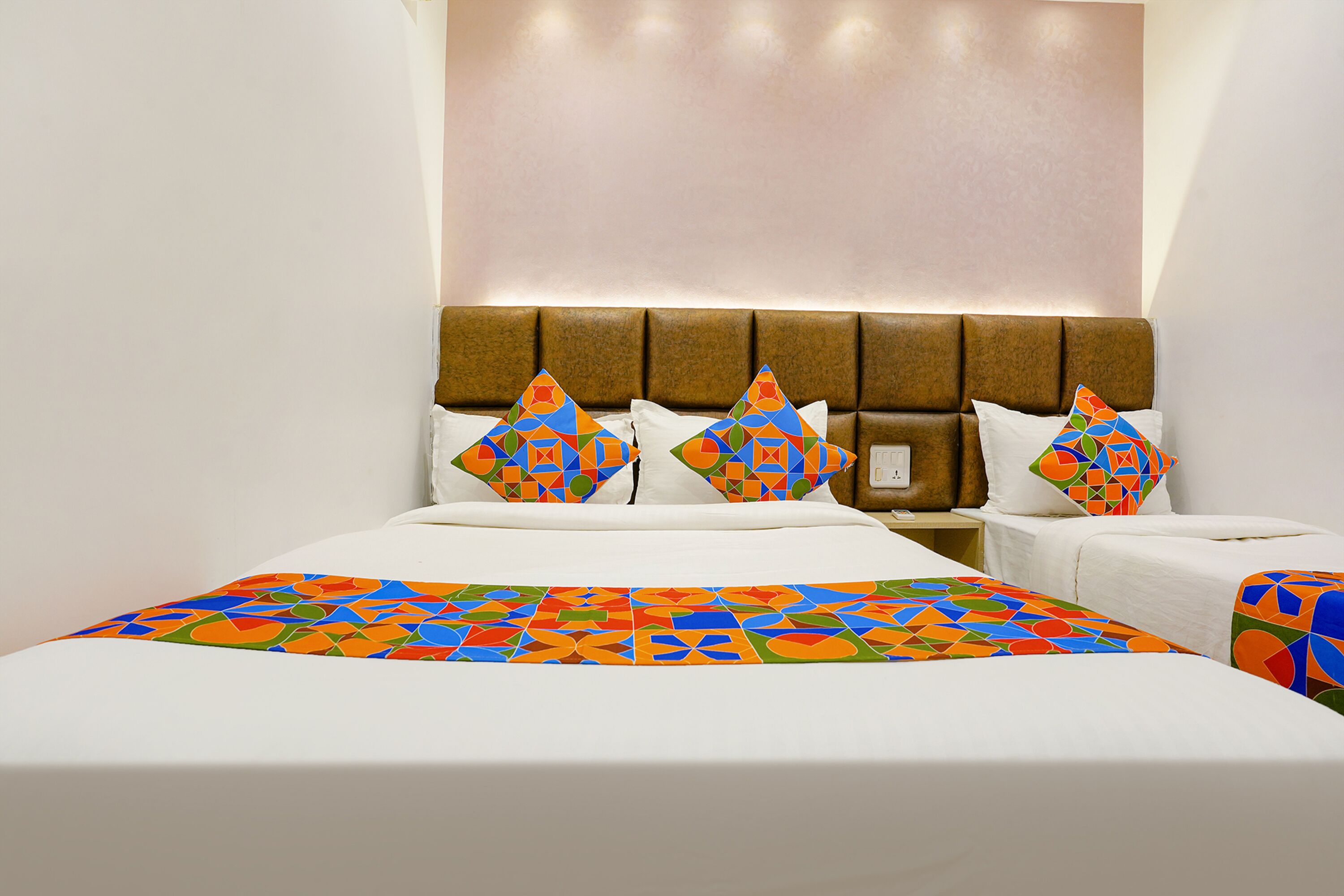 A hotel room with a large bed, two pillows with a colorful geometric pattern, a bedside table, and a headboard with a light panel.