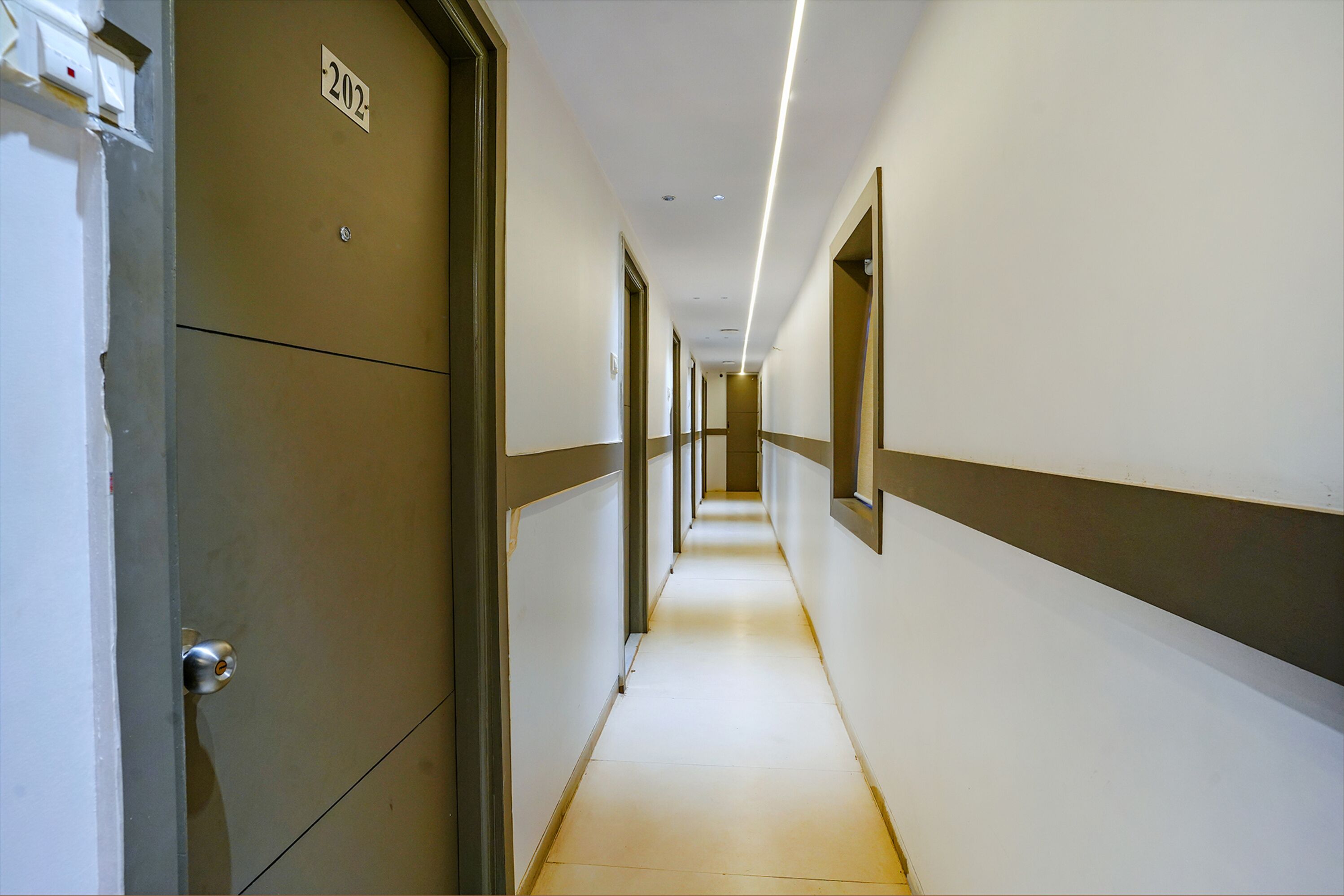 A long, narrow hallway with a door labeled "202" on the left and a light strip running along the ceiling.