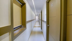 A long, narrow hotel corridor with doors on both sides, a tiled floor, and recessed ceiling lighting. - Fabexpress New Deepak (Mumbai)