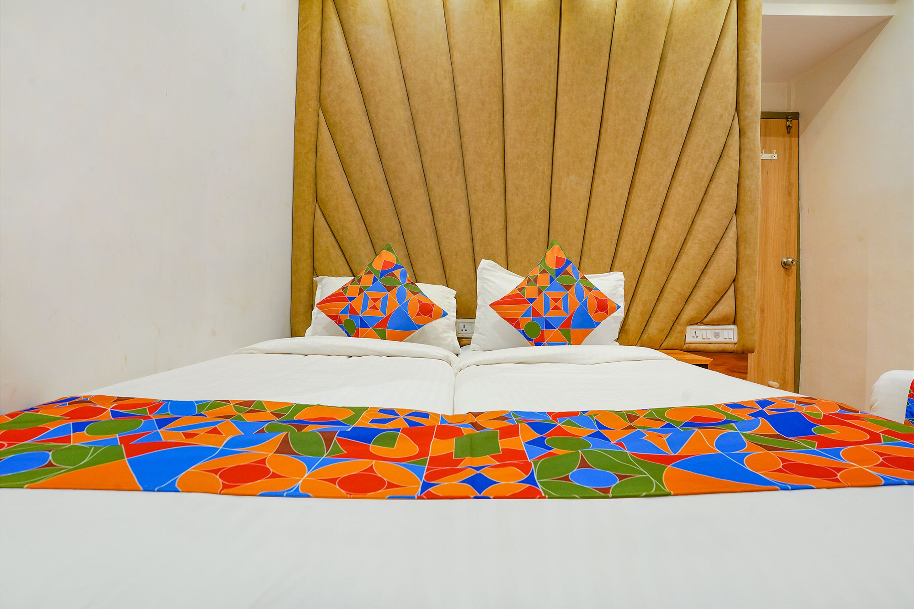 Una cama con un edredón de estampado geométrico colorido, un cabecero de madera y dos almohadas con un diseño geométrico similar.