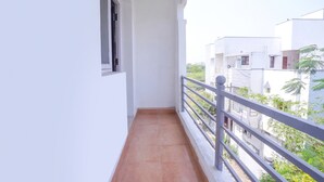 Un balcón estrecho con suelo de baldosas, barandilla blanca y una ventana.