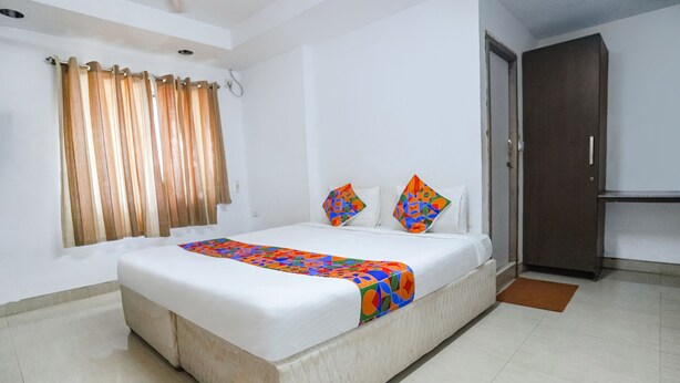 Una cama bien hecha con un edredón colorido, una ventana con cortinas y una puerta cerrada.