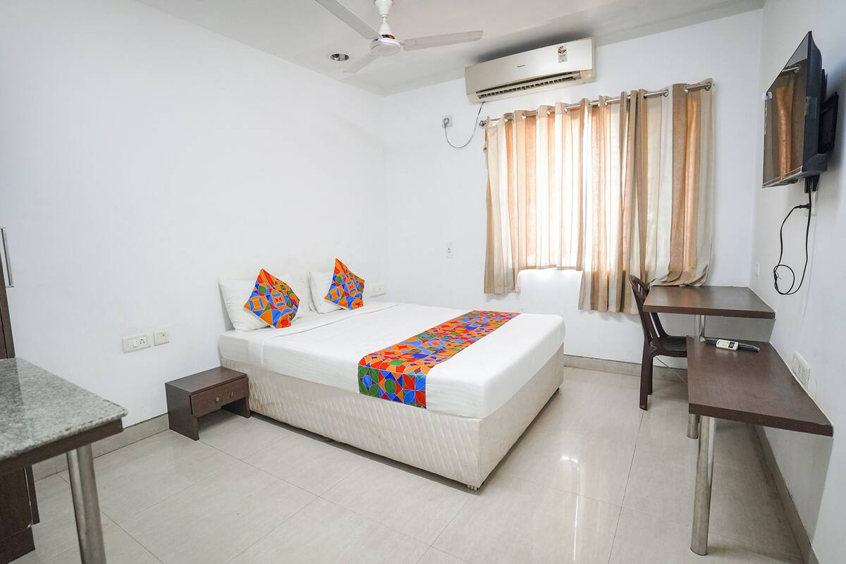 A hotel room with a bed, bedside table, desk, and a ceiling fan.