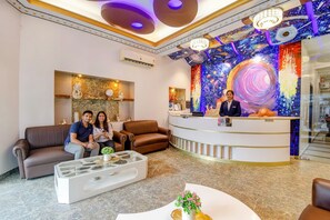 A hotel lobby with a reception desk, seating area, and a colorful mural on the wall. - Fabhotel Prime Rockstar Suites (Kolkata)