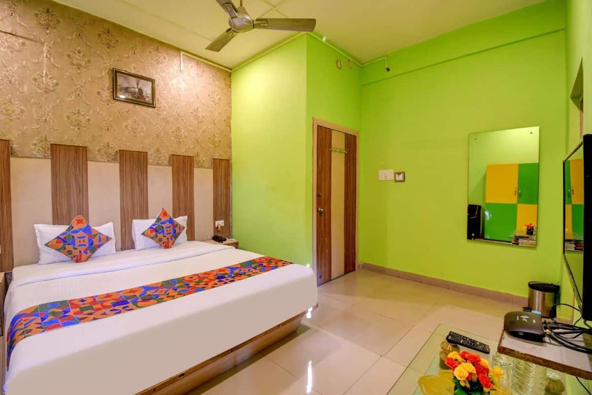 Habitación de hotel con cama, ventilador de techo, pared verde, puerta de madera, espejo y una pequeña mesa con un florero.