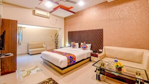 A hotel room with a bed, a sofa, a glass coffee table, and a ceiling fan. - Fabhotel Prime Rockstar Suites (Kolkata)
