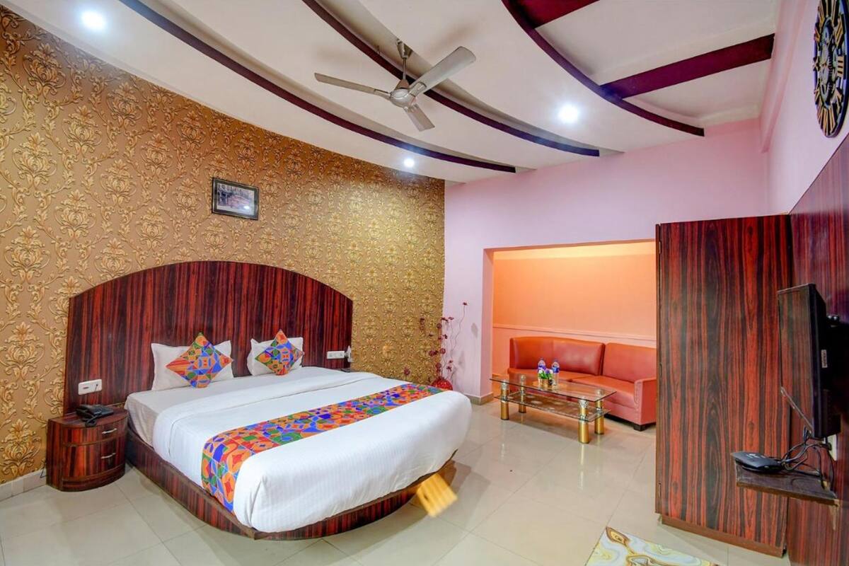 Habitación de hotel con una cama grande, ventilador de techo, televisión y un pequeño rincón de estar con sofá y mesa de centro.