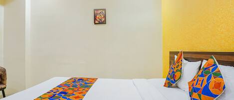 A hotel room with a bed, a colorful bed runner, a painting on the wall, and a chair.