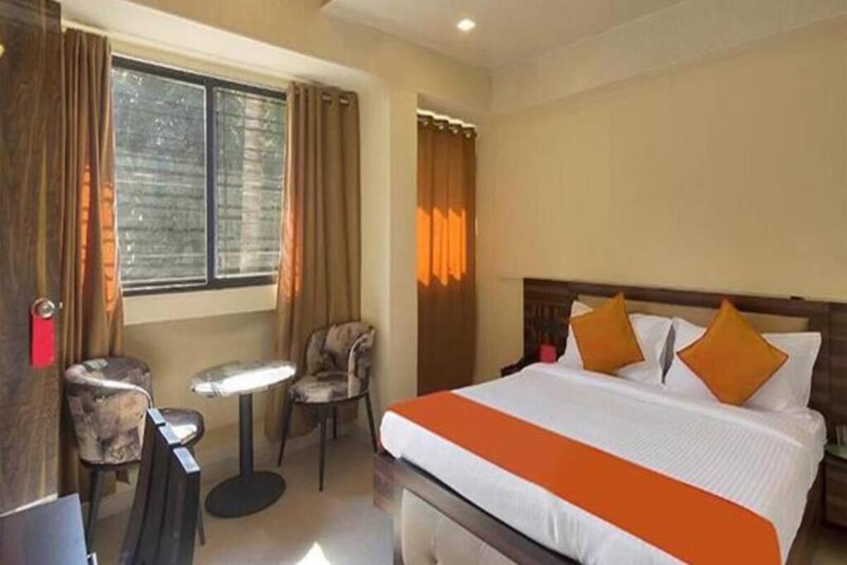 A hotel room with a bed, a small table, two chairs, and a window with curtains.