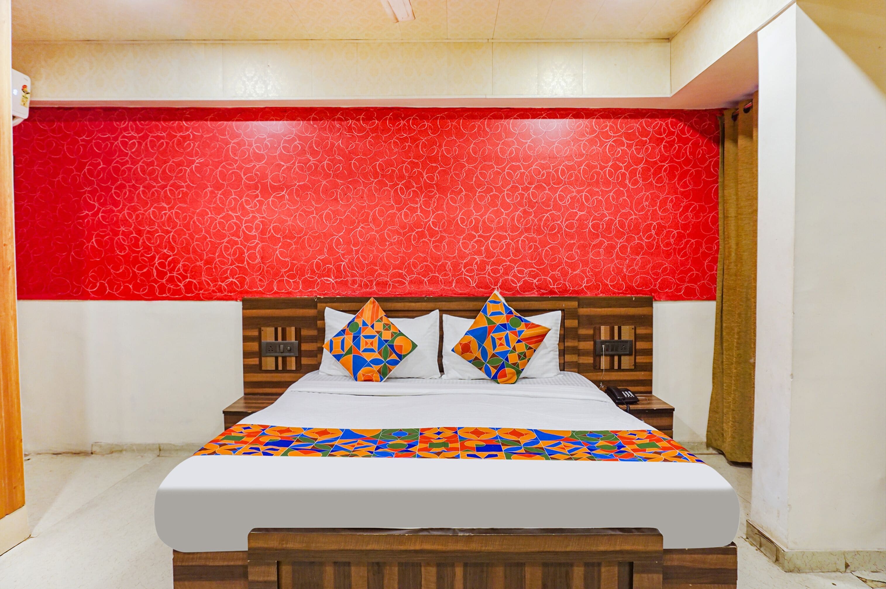 A hotel room with a large bed, a wooden headboard, and a red patterned wall.