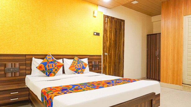 A hotel room with a wooden headboard, a bed with a colorful geometric-patterned bedspread, and a wooden wardrobe. - Fabexpress Gargi Executive (Pune)