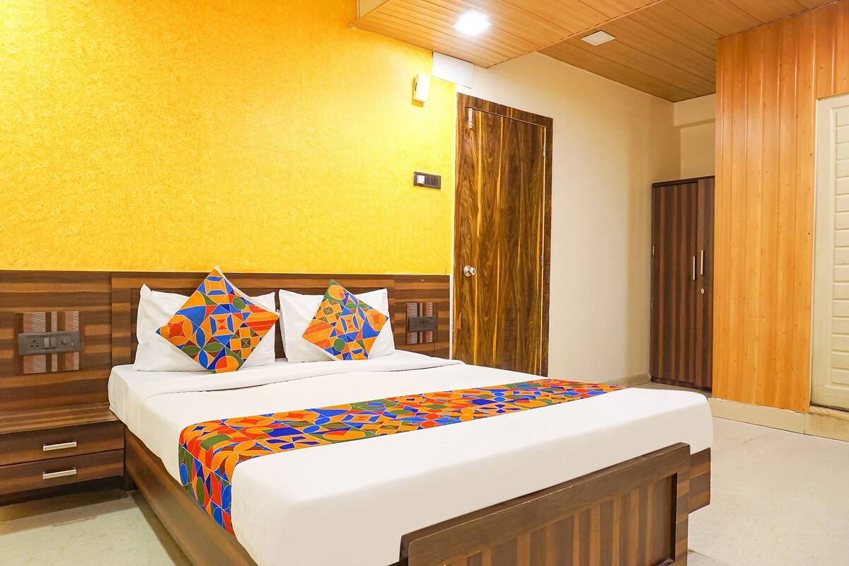 A hotel room with a wooden headboard, a bed with a colorful geometric-patterned bedspread, and a wooden wardrobe.