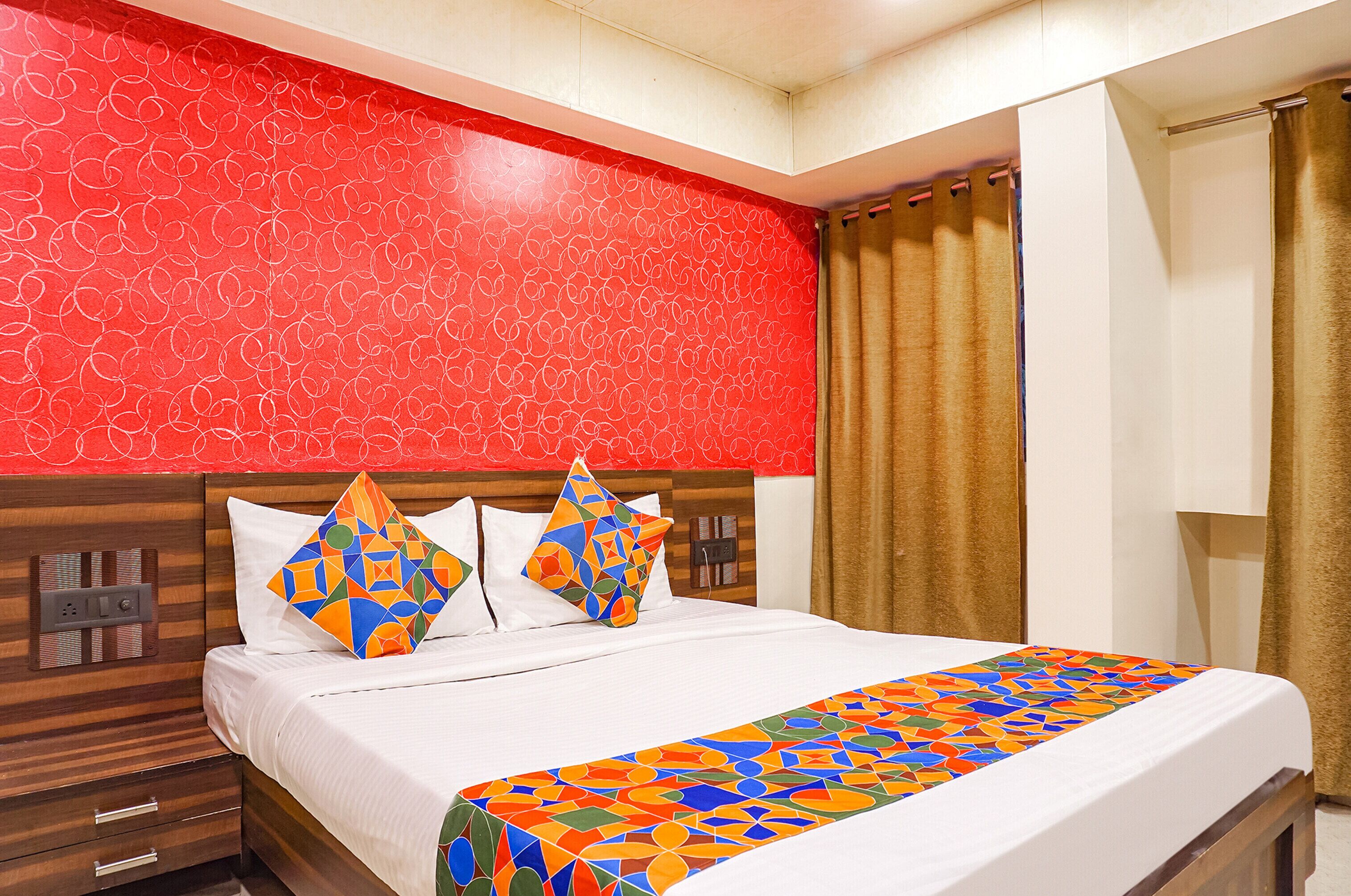 Une chambre d’hôtel avec un lit, un mur à motifs rouges, une tête de lit en bois et une fenêtre avec des rideaux.