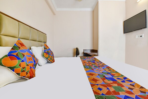 A hotel room with a bed, pillows, a TV, and a patterned runner.