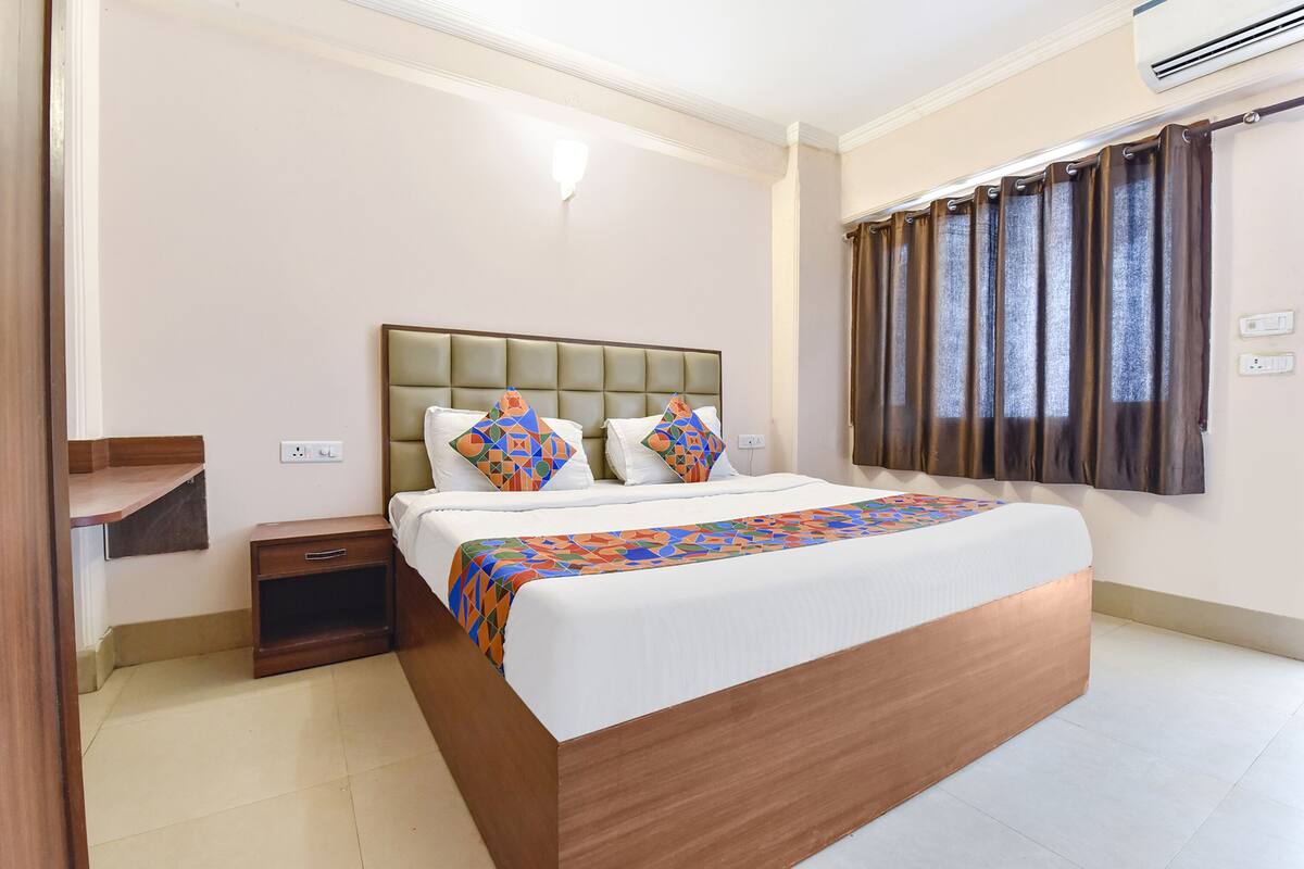 Ein Hotelzimmer mit einem großen Bett, einem Nachttisch, einer Wandaircondition und einem Fenster mit Vorhängen.