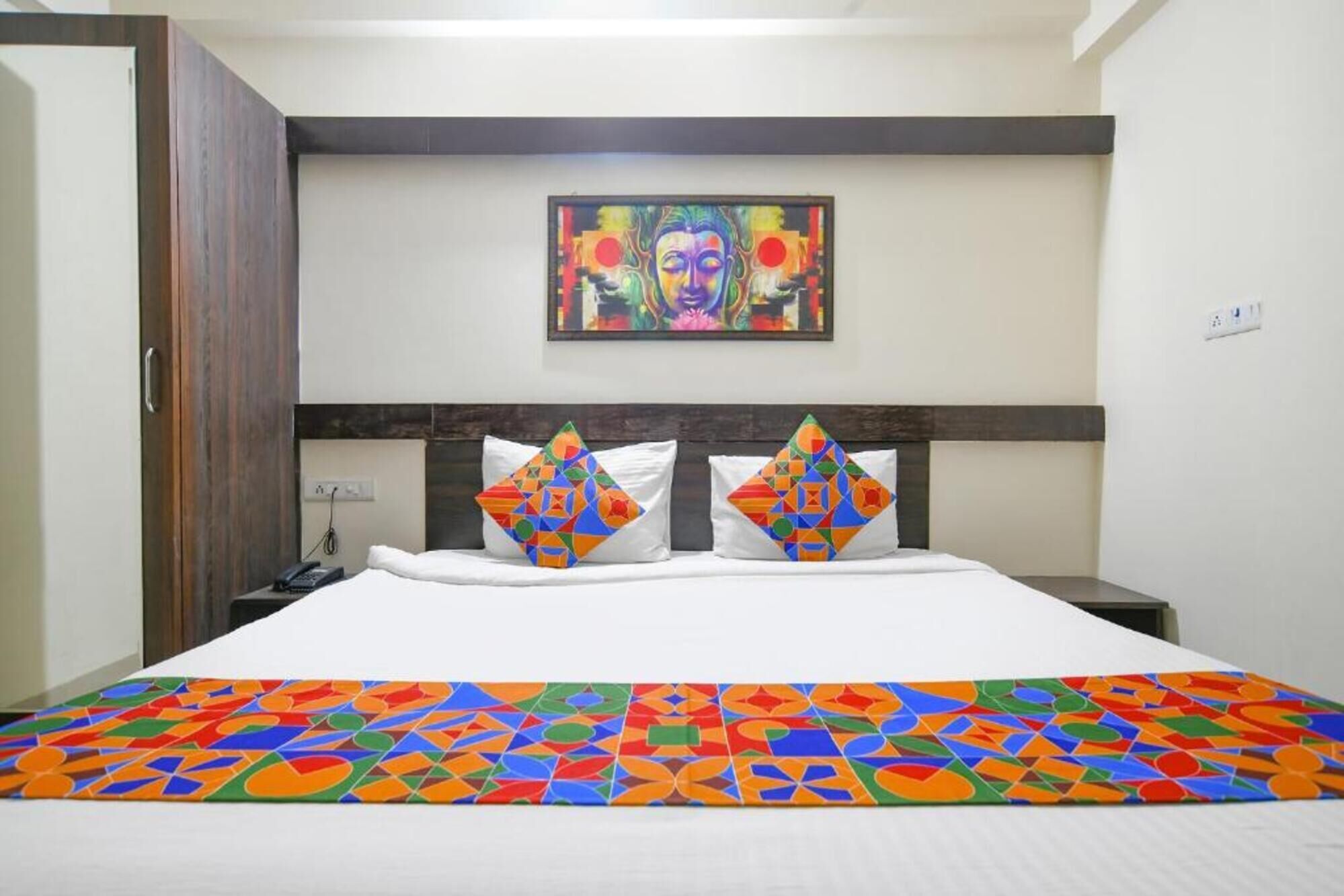 A hotel room with a bed, a nightstand, a painting on the wall, and a door.