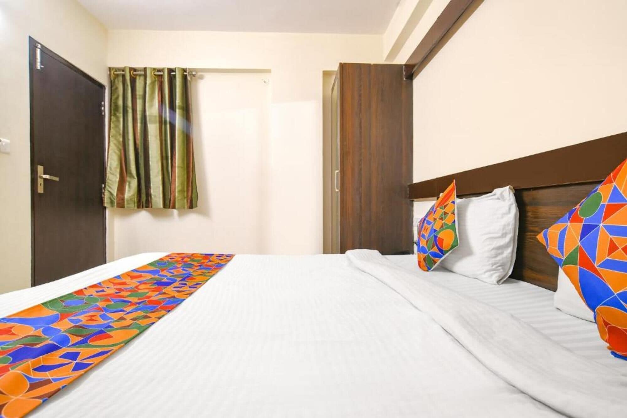 Una habitación de hotel con una cama, una cortina, un armario de madera y una obra de arte colorida sobre la cama.