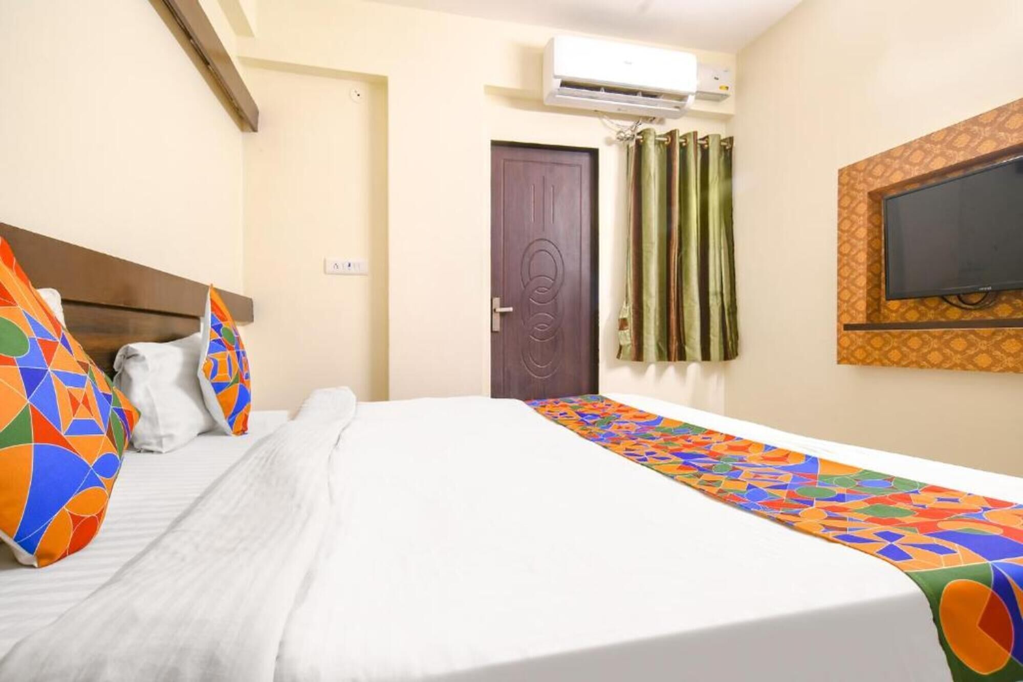 A hotel room with a bed, a TV mounted on the wall, an air conditioning unit, and a door with a curtain.