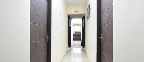 A hallway with two doors, each marked with a number. The hallway is tiled and leads to a room with a window and a door.