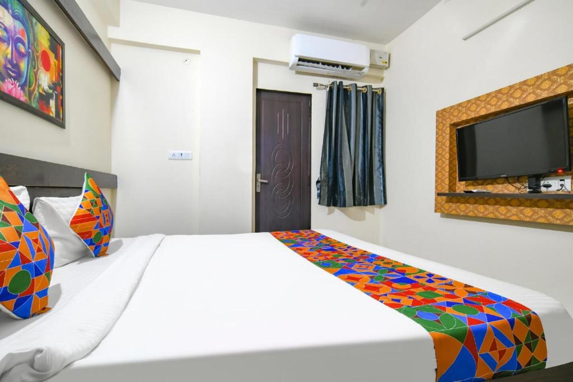 A hotel room with a bed, a TV mounted on the wall, and an air conditioning unit.