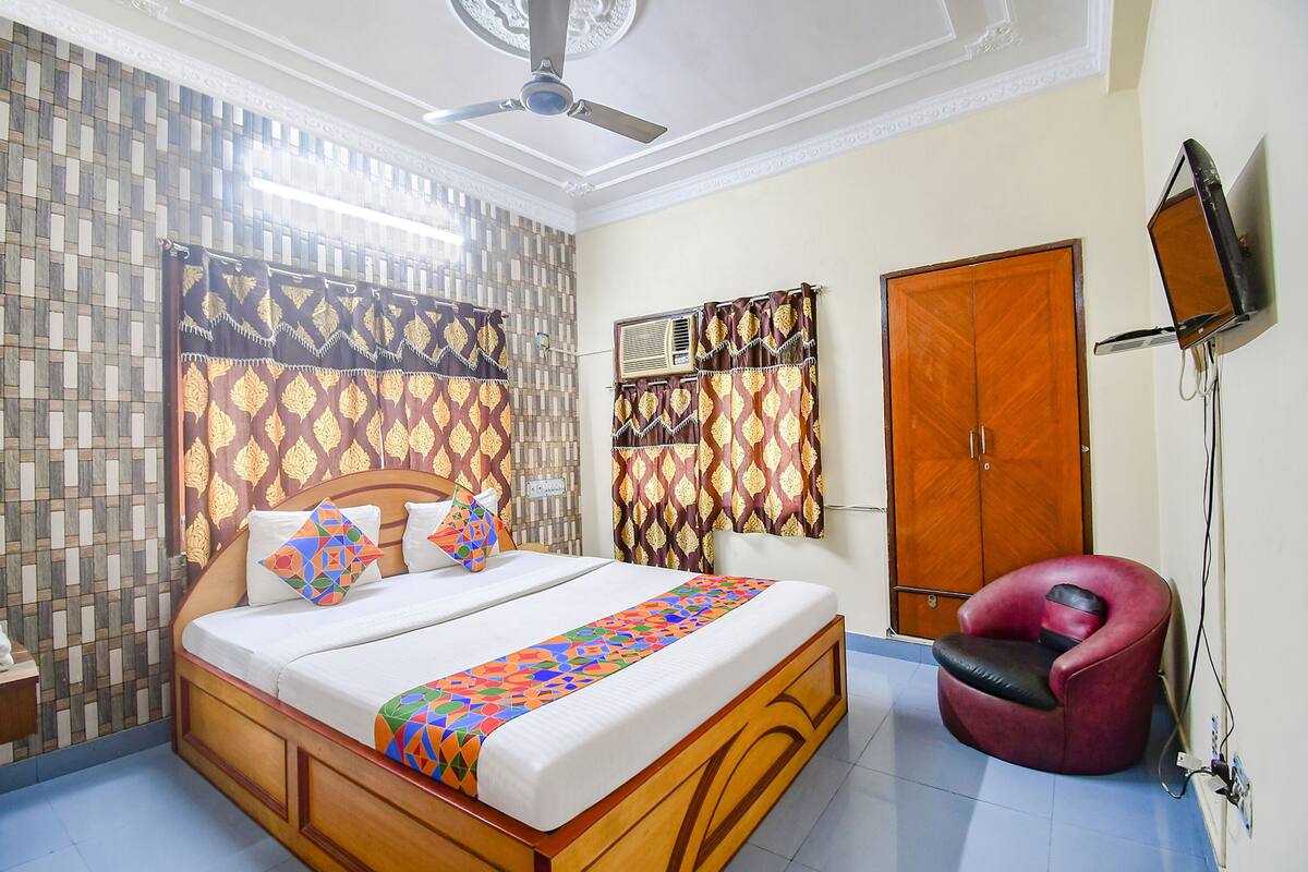 A bedroom with a wooden bed, patterned curtains, a ceiling fan, a wardrobe, and a television mounted on the wall.