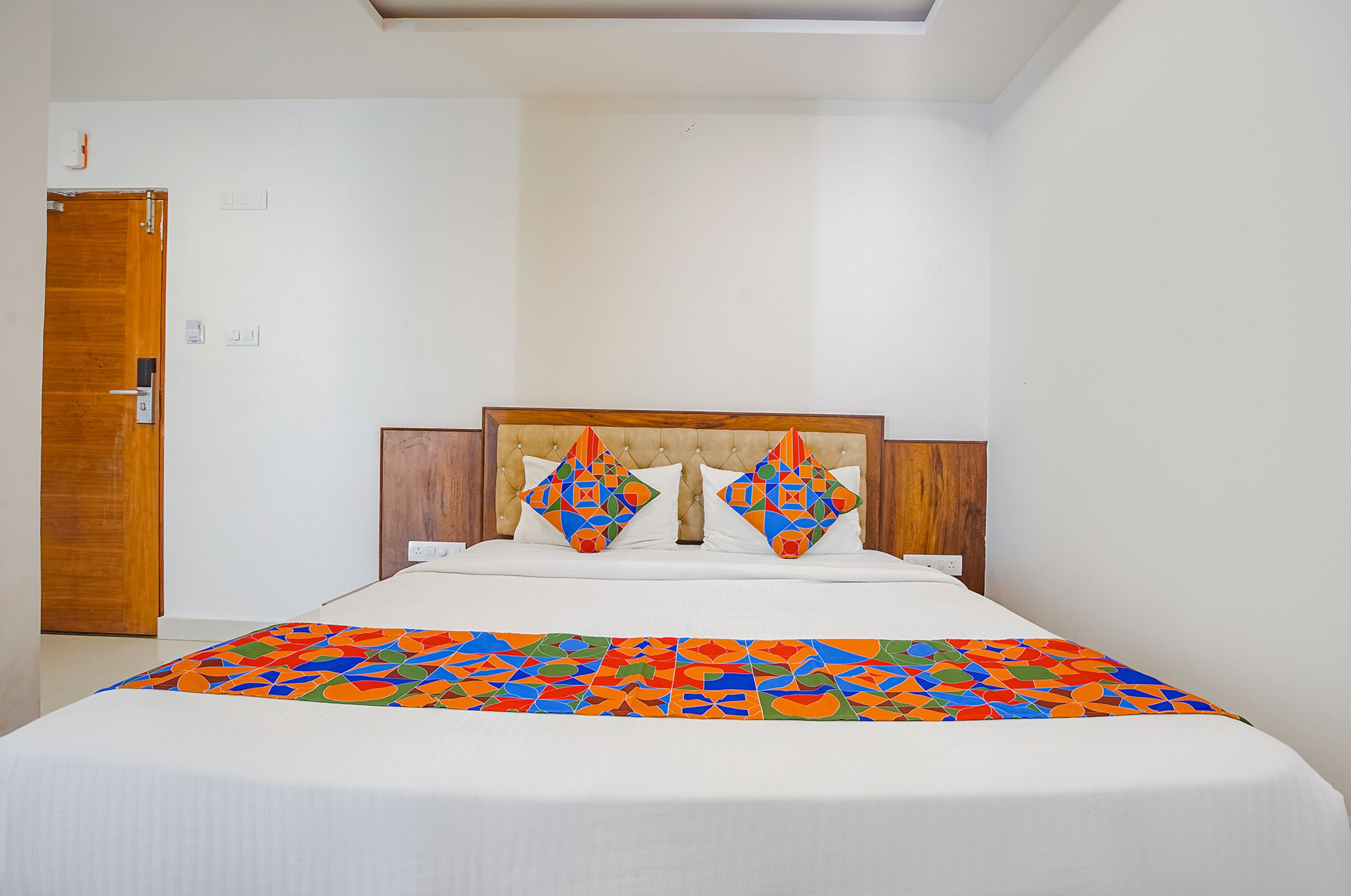 A bedroom with a bed, a wooden door, and a white wall.