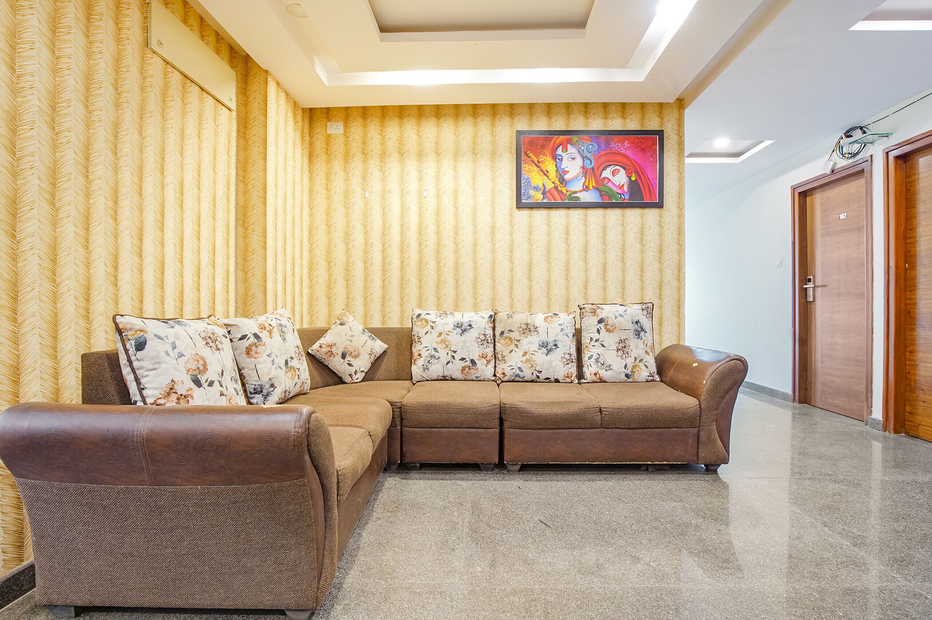 Un salon avec un canapé d’angle marron, des coussins à motifs floraux, un luminaire au plafond et une œuvre d’art encadrée accrochée au mur.