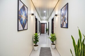 A hallway with framed artwork on the walls, potted plants, and a carpeted floor.