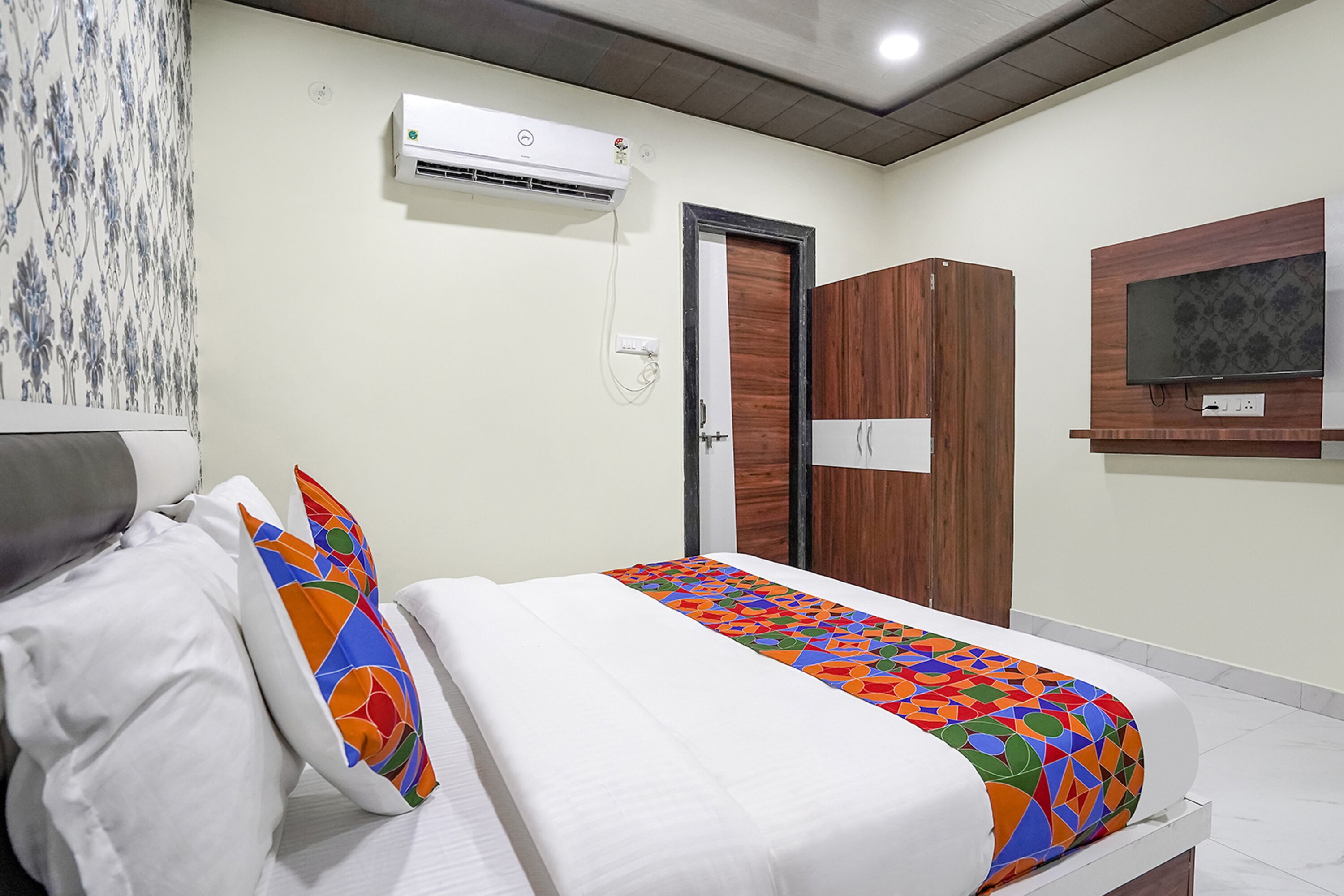 A bedroom with a bed, a TV mounted on the wall, and an air conditioning unit.