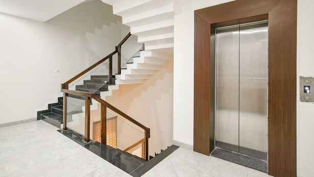 A modern interior with a glass and wooden staircase, a wooden door, and a metallic elevator.