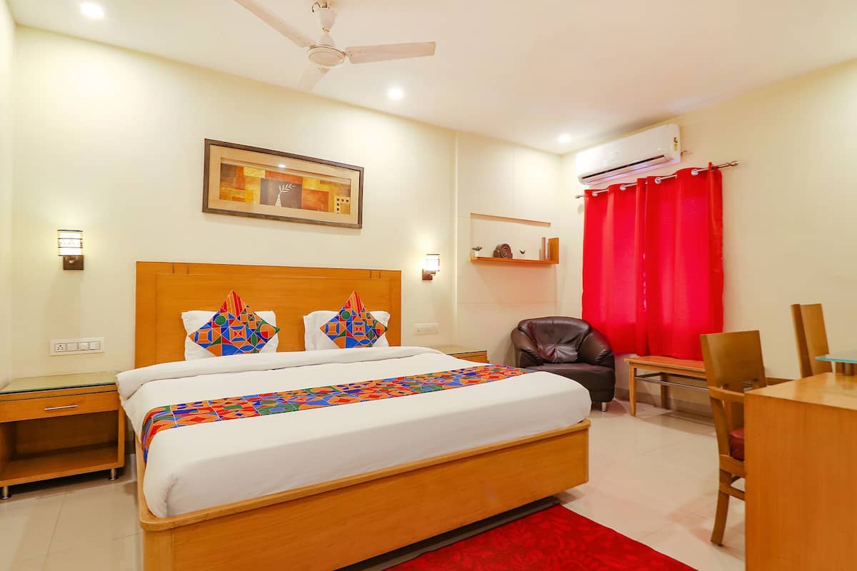 A hotel room with a bed, a desk, a chair, a ceiling fan, an air conditioning unit, and a framed picture on the wall.