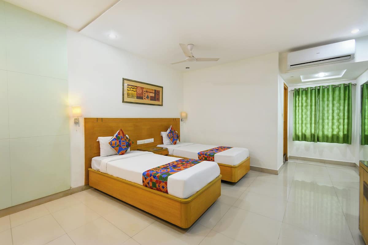 A hotel room with two beds, a ceiling fan, an air conditioning unit, and a green curtain.