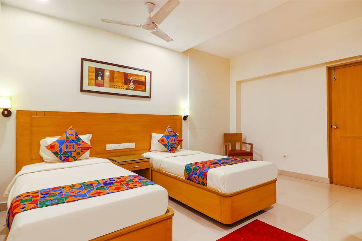 A hotel room with two beds, a ceiling fan, a framed picture on the wall, and a wooden door.