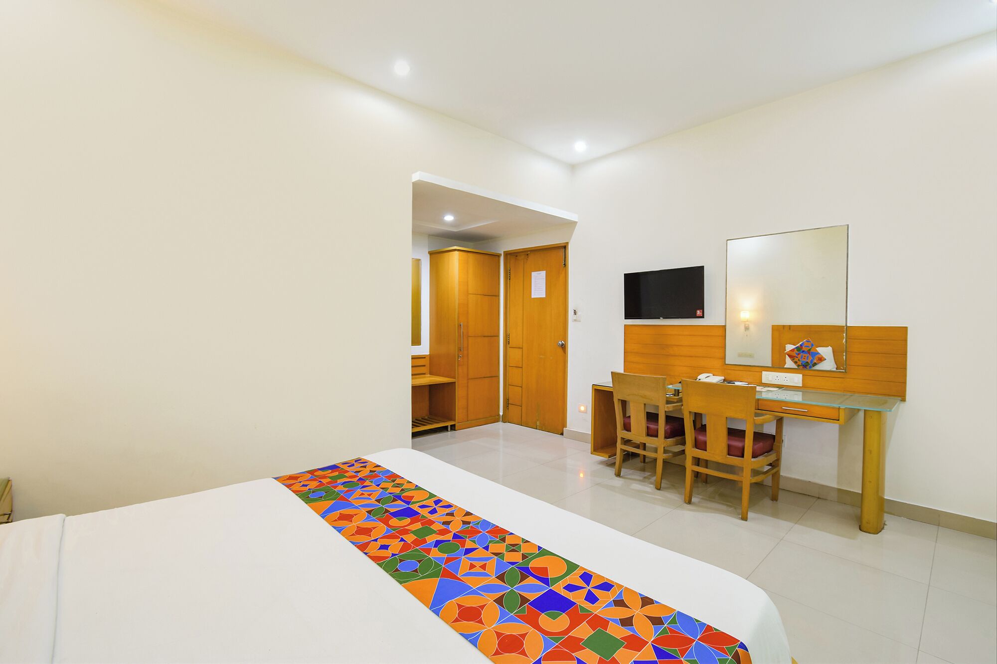 Una habitación de hotel con cama, escritorio, silla, espejo y armario.