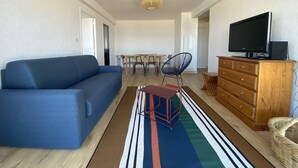 Una sala moderna con un sofá azul, una mesa de comedor con sillas, un televisor sobre un mueble de madera y una alfombra a rayas.