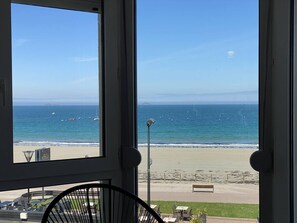 A view from a window overlooking a beach with a clear sky, a bench, and a street lamp. - Apartment with WIFI and Sea View, Trestraou Beach in Perros-Guirec (Perros-Guirec)