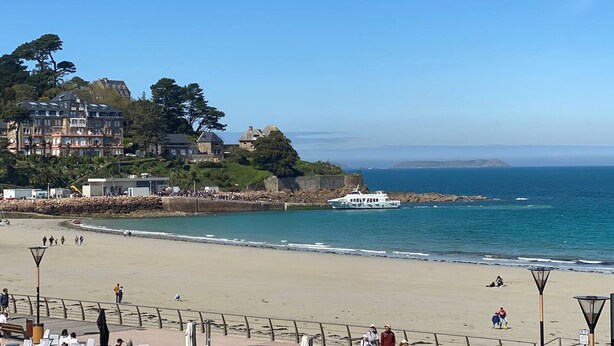 Una playa con un muro de piedra, un barco y edificios al fondo.