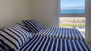 Una habitación con una cama con ropa de cama a rayas, un ventanal con vista al mar y un balcón con mobiliario exterior.