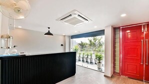 A reception area with a black counter, a ceiling fan, a red door, and a view of the outdoors through a large window. - Fabhotel Lupin International (Udaipur)