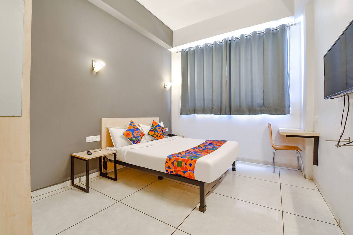 Habitació d'hotel amb llit, taula de nit, cadira i televisió penjada a la paret.