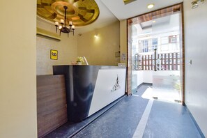 A hotel reception area with a modern design, including a reception desk, a chandelier, and a glass door leading outside. - Fabhotel Resolute (Jaipur)