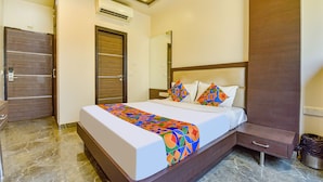 A hotel room with a bed, a nightstand, a drawer, a mirror, and an air conditioning unit. - Fabhotel Resolute (Jaipur)